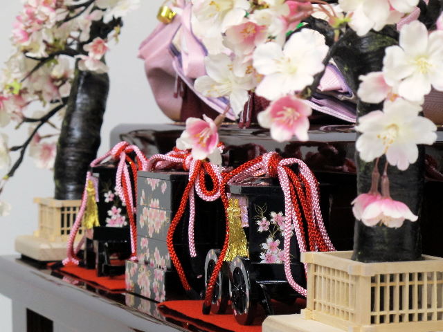 落ち着いた紫グラデーションに桜刺繍のアクセントが入った渋めの雛人形を落ち着いた茶塗りの三段に並べました。屏風と台の柄は金桜で重厚な中にも華やかさがあります。