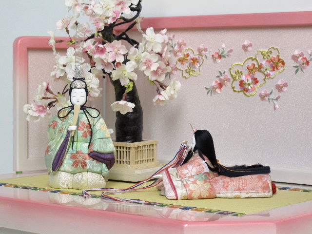 淡い色合いの桜柄衣装の座りと立ちの雅な木目込み人形をかわいいホワイトピンク収納台に桜で飾りました。