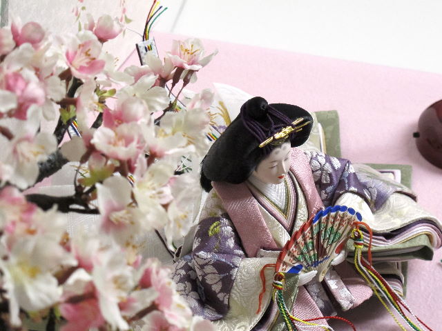 落ち着いた色合いの重ねと桜模様の衣装が特徴のお雛さまを桜屏風の前に大きな桜の木と共に優雅に飾りました。桐箱に収める便利な収納タイプです。
