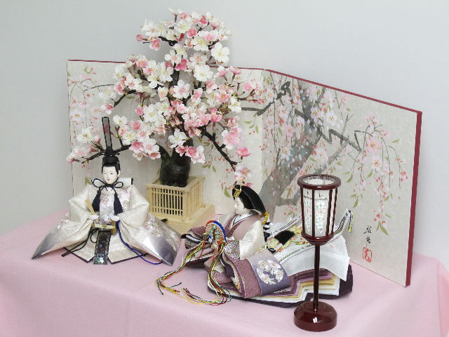 ちょっと渋めの紫のグラデーションと重ね、明るい桜の刺繍がアクセントになった品の良い雛人形を桜屏風の前に大きな桜の木と共に優雅に飾りました。桐箱に収める便利な収納タイプです。
