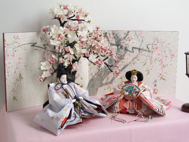 淡いピンクと紫のお雛様を桜屏風の前に大きな桜の木と共に優雅に飾りました。桐箱に収める便利な収納タイプです。