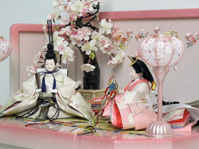 桜の刺繍が特徴の姫はピンク、殿はグリーンのグラデーションが綺麗なお雛さまをかわいいホワイトピンク収納台に桜で飾りました。
