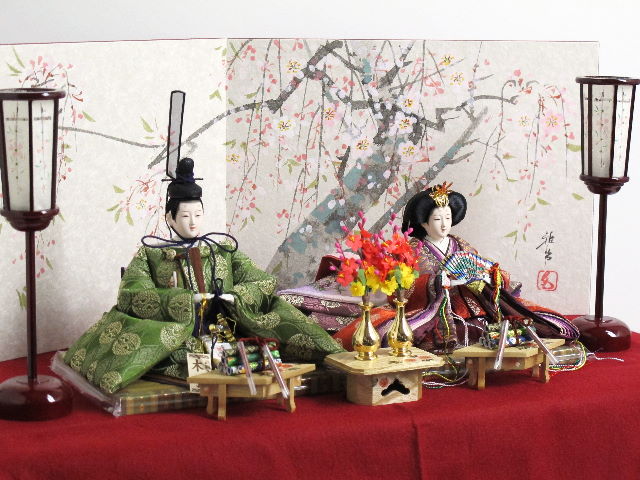 平安貴族の愛用した有職文様、鶴の丸を正絹衣装に織り込み着せ付けた落ち着いたお雛さまを桐箱を台として手描きの桜屏風で飾りました。便利な収納タイプです。