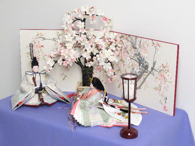 薄緑と紫の落ち着いた正絹衣装の雛人形を桜屏風の前に大きな桜の木と共に優雅に飾りました。桐箱に収める便利な収納タイプです。
