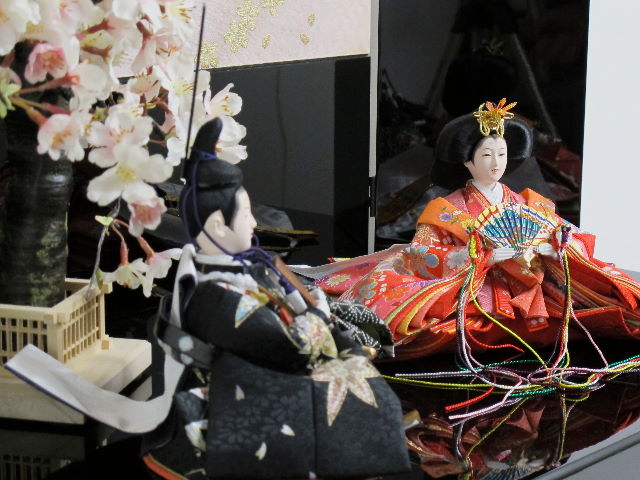 女雛は赤、男雛は黒。かわいい色合いの友禅衣装のお雛さまを桜吹雪をデザインした黒塗りの収納箱と組み合わせました。