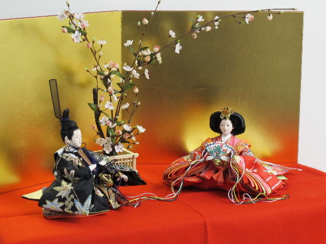 女雛は赤、男雛は黒。かわいい色合いの友禅衣装のお雛さまを向かい合わせに白梅の木と並べます。