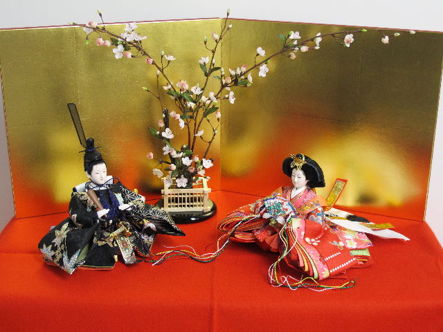 女雛は赤、男雛は黒。かわいい色合いの友禅衣装のお雛さまを向かい合わせに白梅の木と並べます。