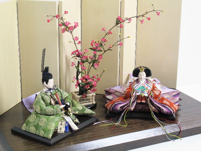 平安貴族の愛用した有職文様、鶴の丸を正絹衣装に織り込み着せ付けた落ち着いたお雛さまです。女雛と男雛の間に紅梅の木を置くシンプルな飾りです。