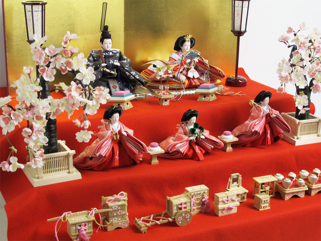 嫁入り道具が揃った並べて楽しむ雛人形です。収納式の三段台に赤毛氈を敷いて金屏風と並べます。