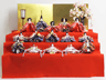 緋毛氈、金屏風で小さい十五人揃いを収納式の三段台に並べたコンパクトな雛人形です。