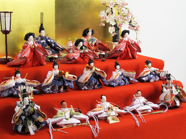 緋毛氈、金屏風で小さい十五人揃いを収納式の三段台に並べたコンパクトな雛人形です。