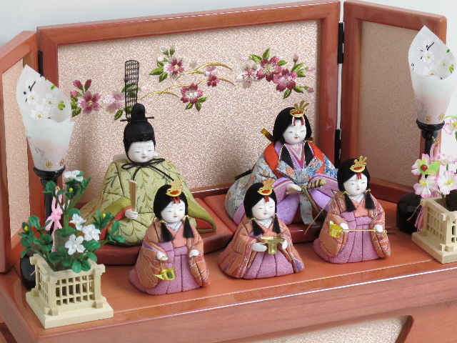 落ち着いた衣装の木目込み人形の五人飾りです。桜柄の刺繍がポイントのピンク色の収納台に飾りました。