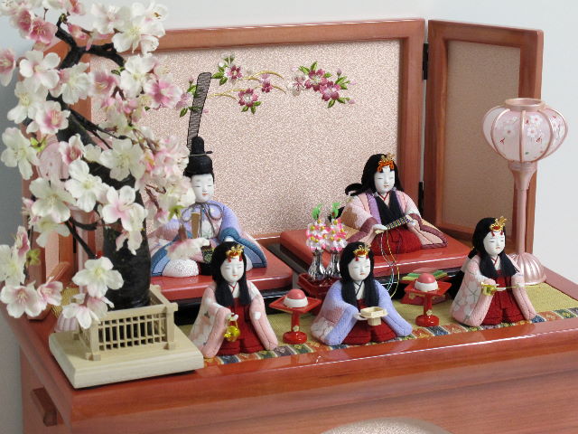 パステルカラーの衣装がかわいい木目込み人形の五人揃いです。桜の刺繍がポイントのパールローズピンクの収納台に飾りました。
