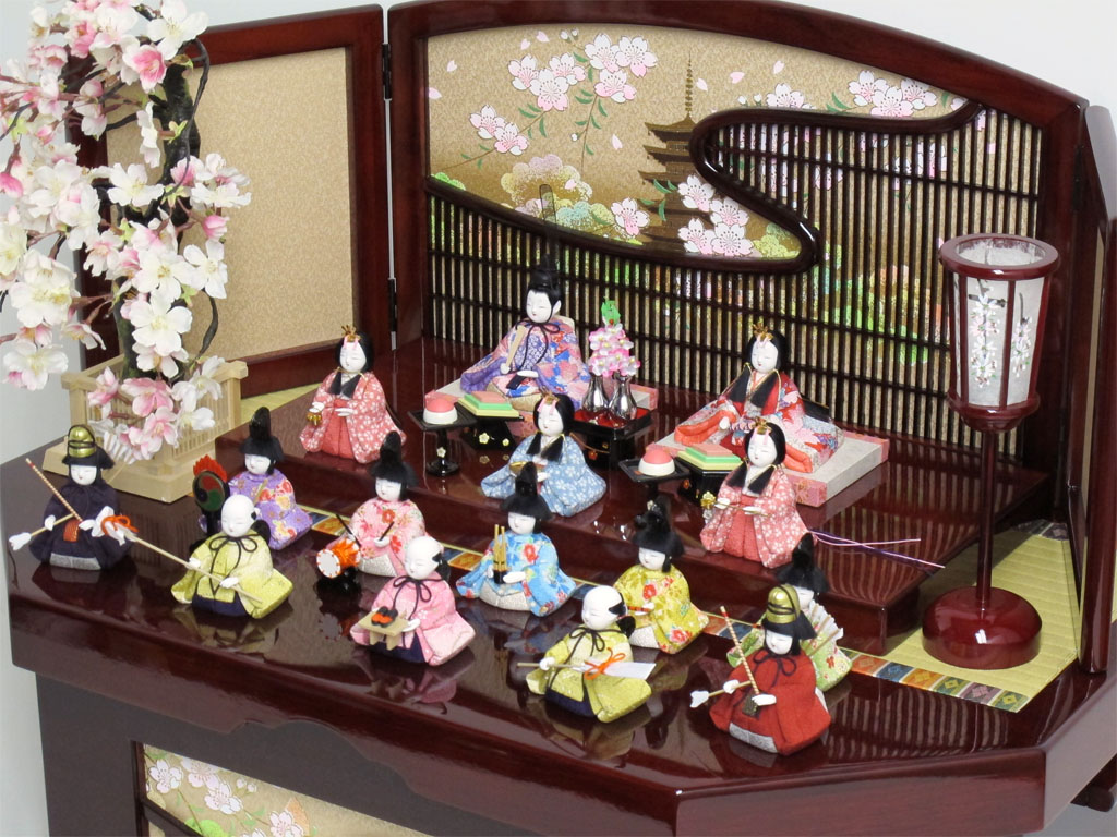 ちいさくてかわいい木目込み人形の十五人揃いです。桜柄の友禅衣装雛を重厚な春慶塗の収納式六角台に所狭しと並べます。