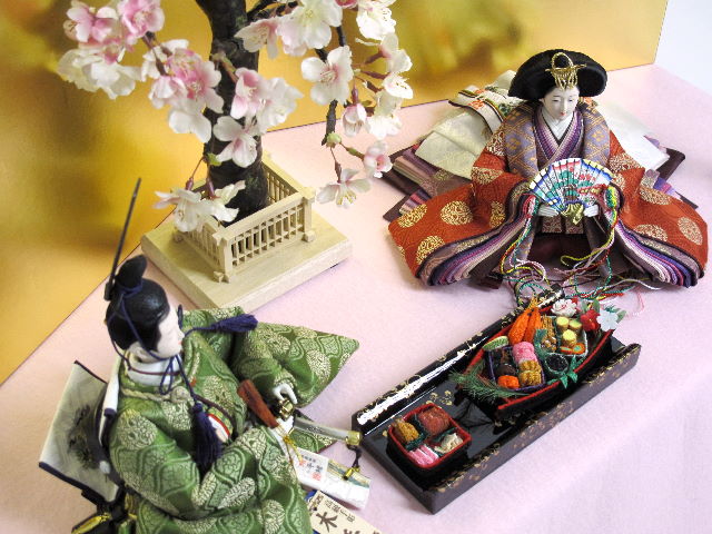 平安貴族の愛用した有職文様、鶴の丸を正絹衣装に織り込み着せ付けた落ち着いたお雛さまをピンクの毛氈で桐箱の上に金屏風で飾りました。