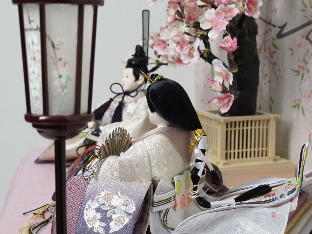 ちょっと渋めの紫のグラデーションと重ね、明るい桜の刺繍がアクセントになった品の良い雛人形を桜屏風の前に大きな桜の木と共に優雅に飾りました。桐箱に収める便利な収納タイプです。