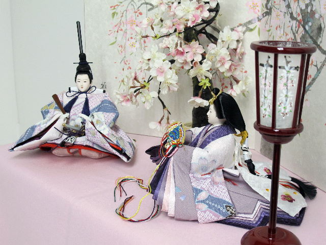 この小ささでも上仕立て。コンパクトでも上質。高貴な紫を重ねや唐衣に用いた雛を枝垂桜と桜絵屏風で優雅に飾った桐箱収納式のひな人形です。