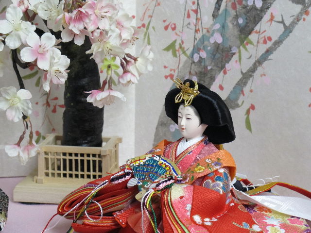 女雛は赤、男雛は黒。かわいい色合いの友禅衣装のお雛さまを枝垂桜と桜絵屏風で優雅に飾った桐箱収納式のひな人形です。