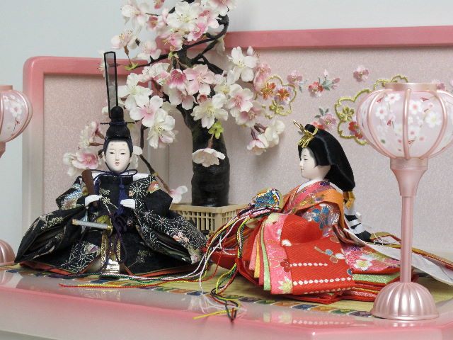 女雛は赤、男雛は黒。かわいい色合いの友禅衣装のお雛さまをかわいいホワイトピンク収納台に桜で飾りました。