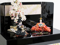 女雛は赤、男雛は黒。かわいい色合いの友禅衣装のお雛さまを桜吹雪をデザインした黒塗りの収納箱と組み合わせました。