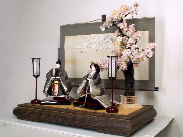 深い色合いの大島紬が落ち着きを表現し、桜の木と掛け軸が雛人形に彩りを添える立ち雛親王飾り