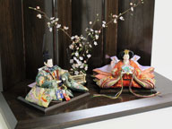 平安を意味する鳳凰を刺繍の柄とした豪華なお雛さまです。茶塗りの屏風と台に白梅の木を中央に置くシンプルな飾りです。
