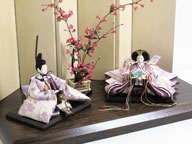 淡い紫地に紫の桜を正絹衣装に織り込んだ優雅で高貴なお雛さまです。女雛と男雛の間に紅梅の木を置くシンプルな飾りです。