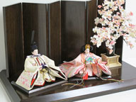 桜色のおひなさまを茶塗り台に置いて、大きな桜の木で引き立てたシンプルな飾りです。